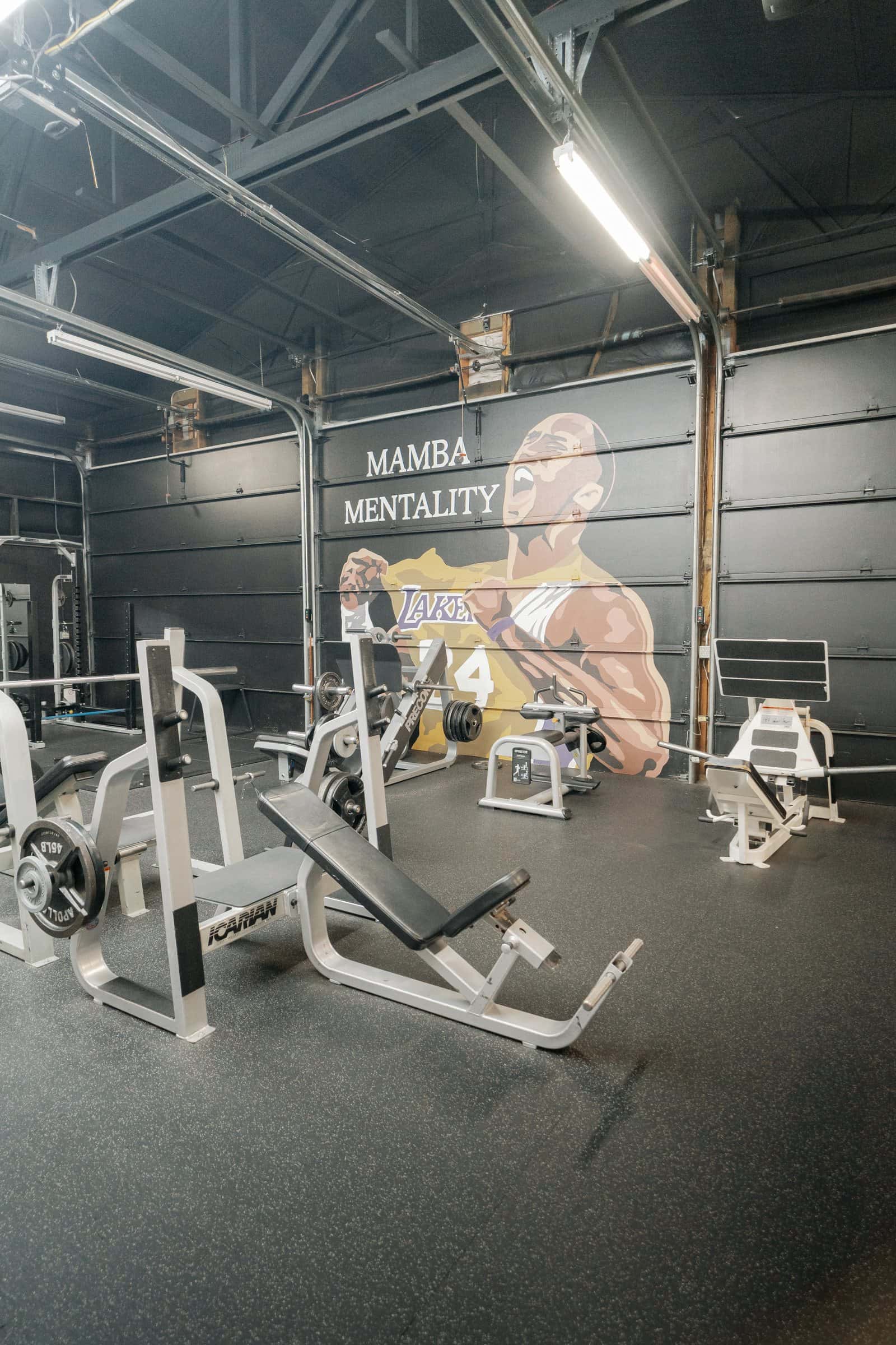 Free weights: benches and plate-loaded machines by the Mamba Mentality mural