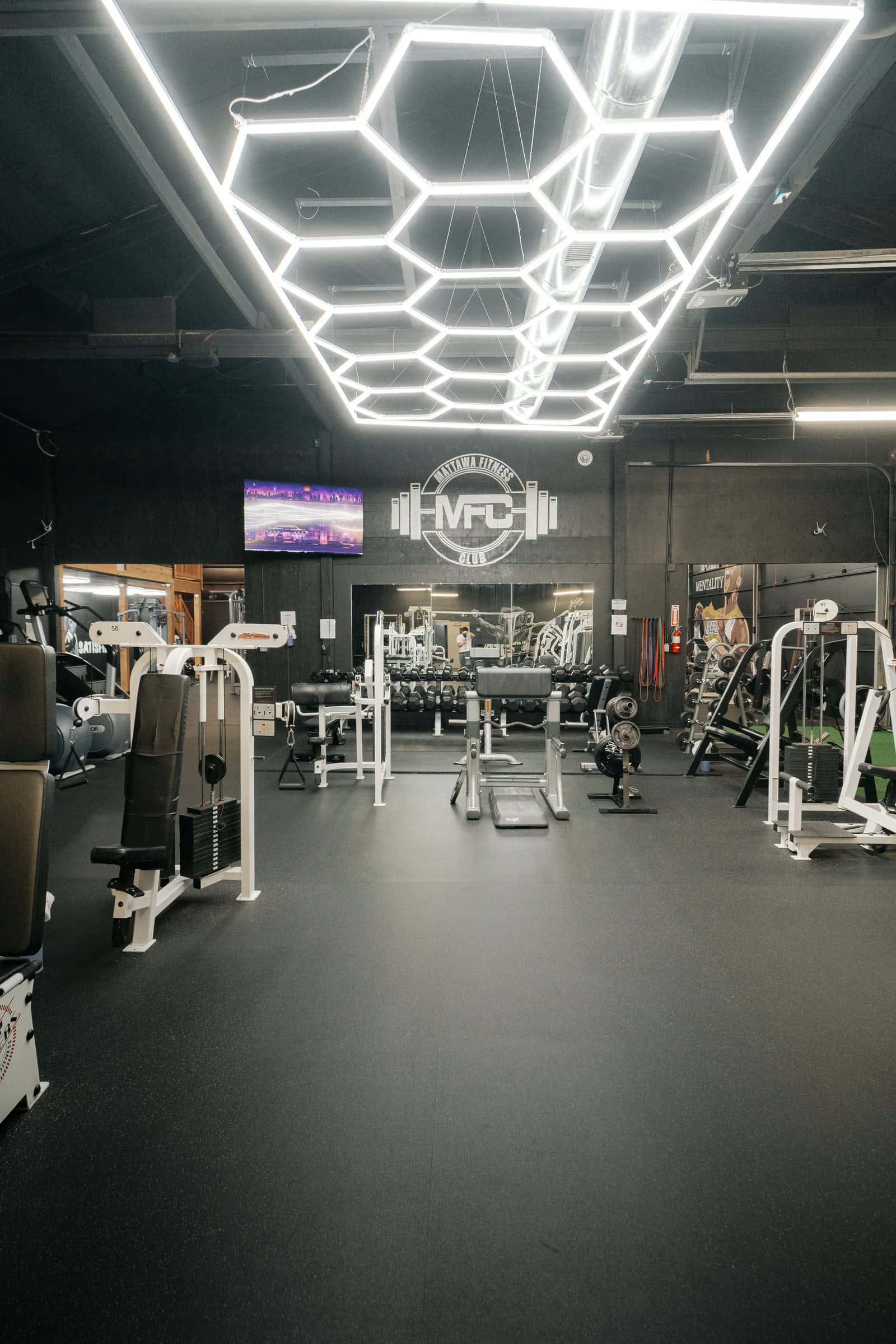 Main workout area: machines on a black floor under hexagon LED ceiling lights