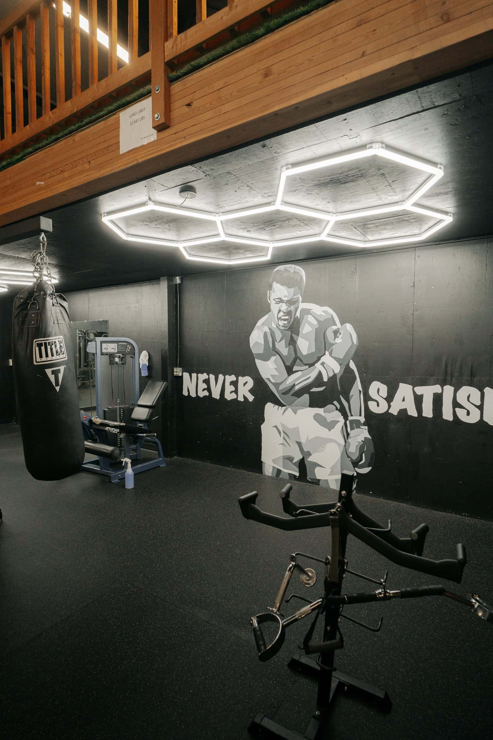 A cable station and a heavy bag in front of the Never Satisfied mural, under hexagon lights