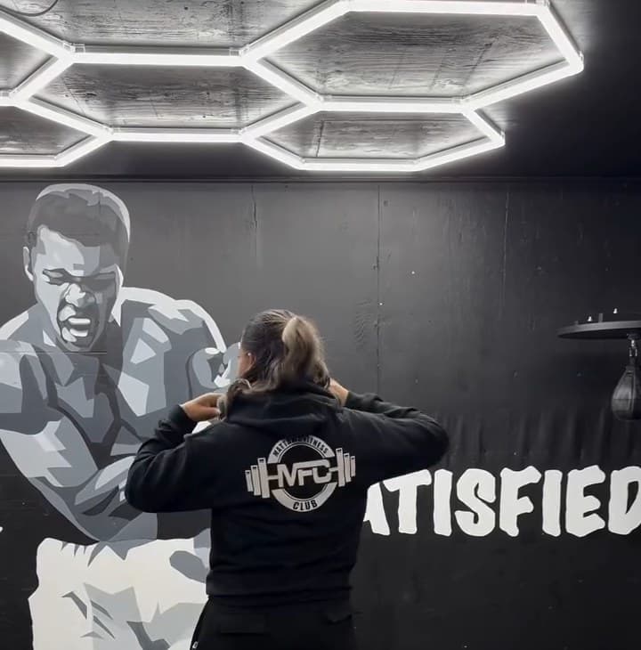 Back of the black MFC hoodie with the white Mattawa Fitness Club logo, in front of the Never Satisfied mural